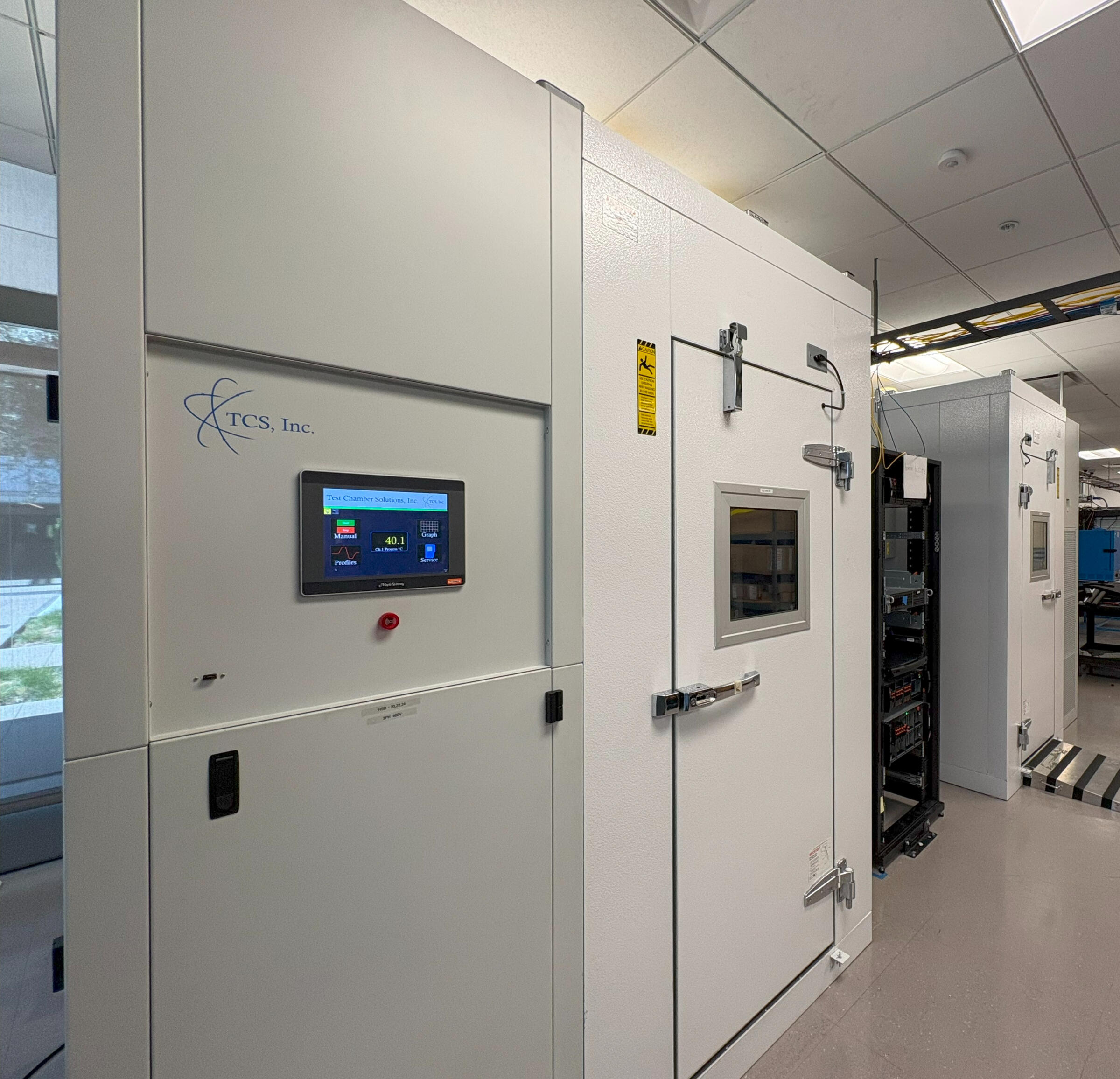 Custom Walk-In Environmental Test Chambers by TCS, Inc. A row of custom-built walk-in environmental test chambers with durable gray and yellow finishes, featuring diamond-plated doors and advanced control panels for precision testing in a high-performance lab setting.
